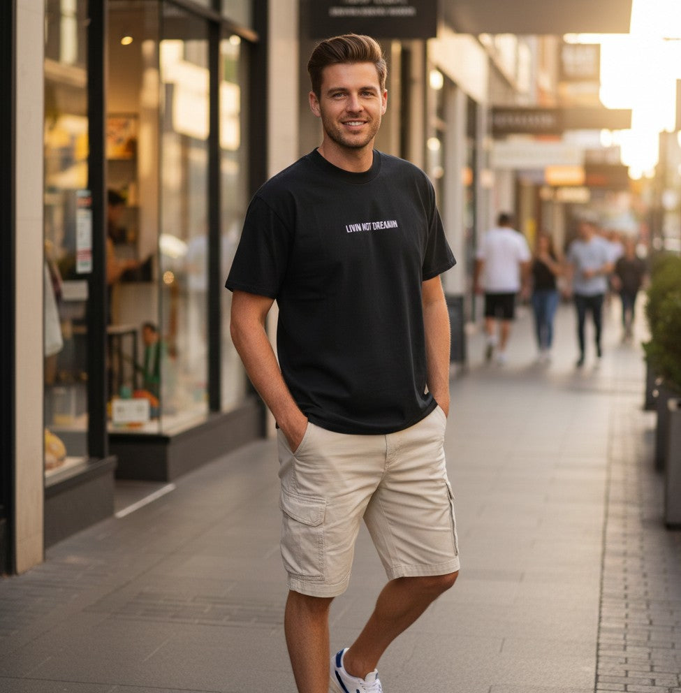 Man wearing the charcoal Livin’ not Dreamin’ Classic Tee with beige shorts in a city shopping precinct.